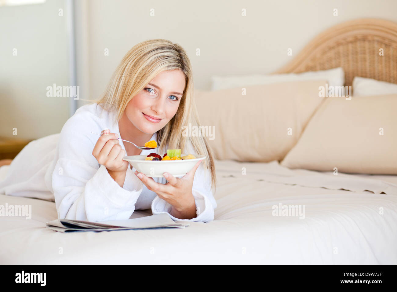 gesunde junge Frau Essen Obstsalat auf Bett Stockfoto
