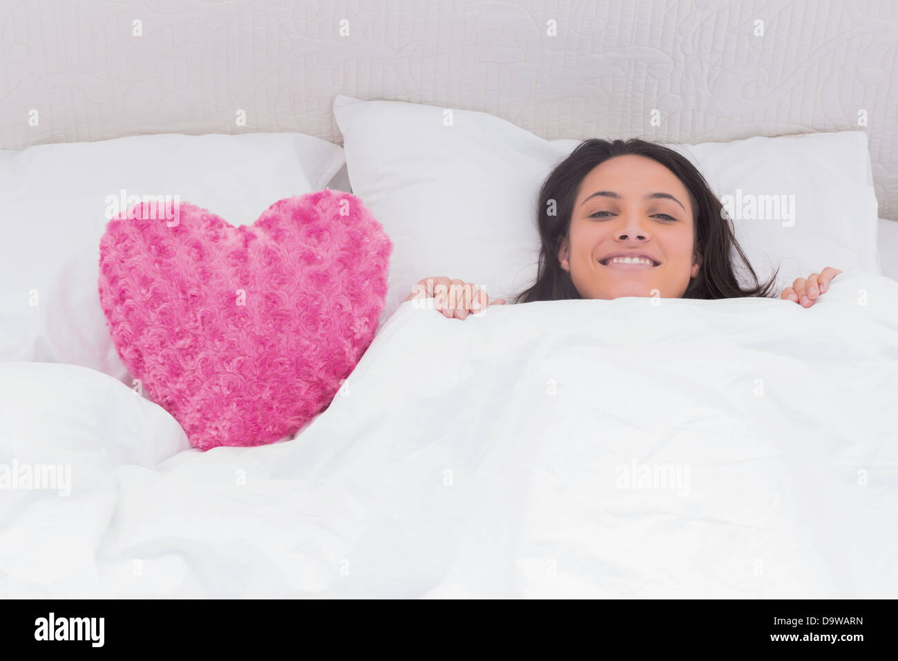 Frau im Bett neben einem flauschigen Herz Kissen liegend Stockfoto