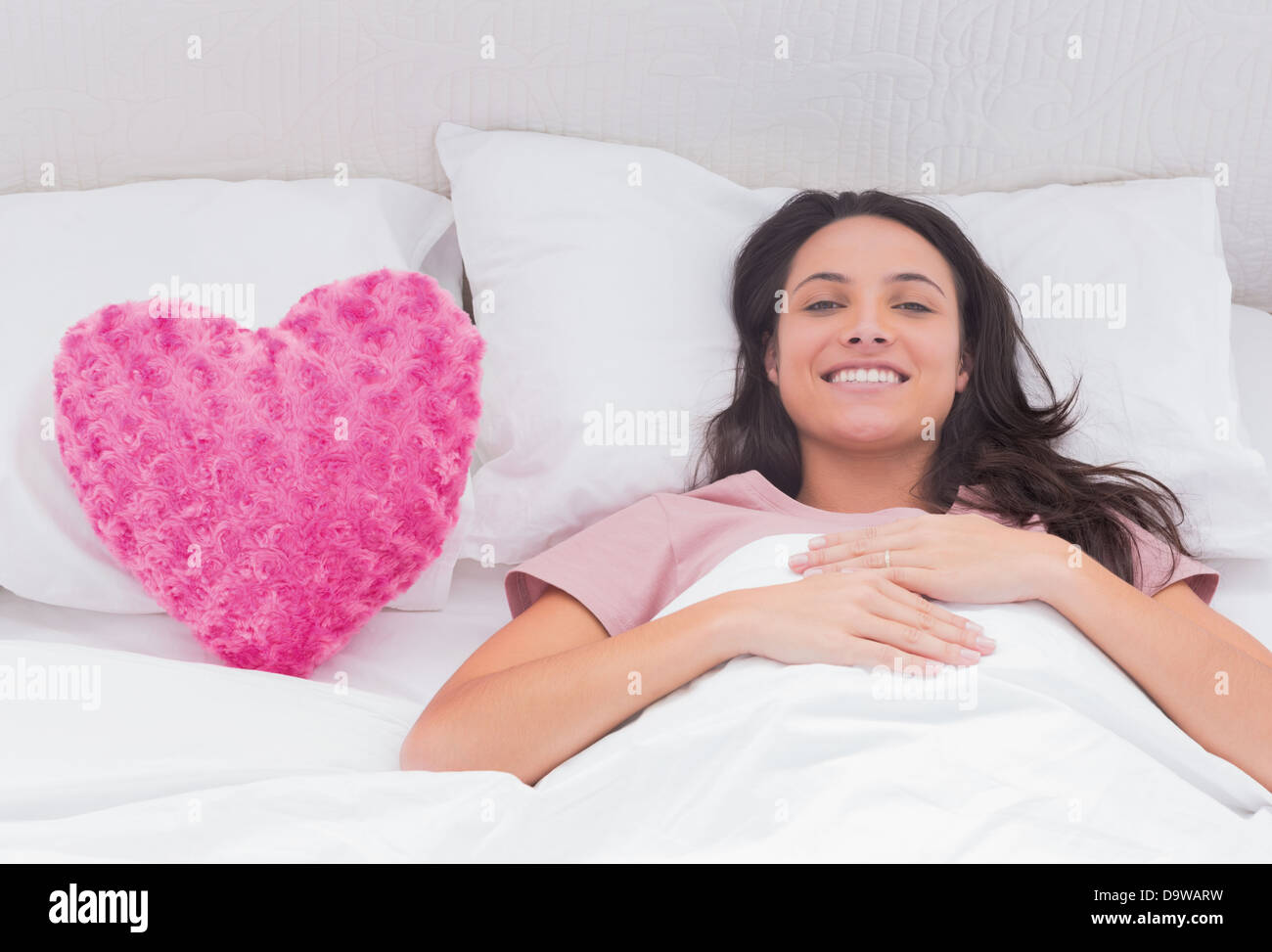 Frau liegt in ihrem Bett neben einem rosa Herz-Kissen Stockfoto