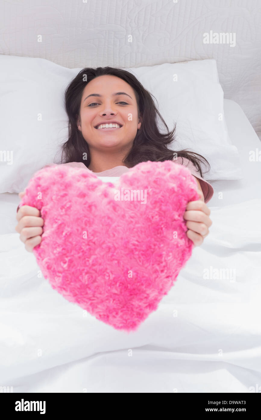 Frau in ihrem Bett liegen und halten eine flauschige Herz Kissen Stockfoto