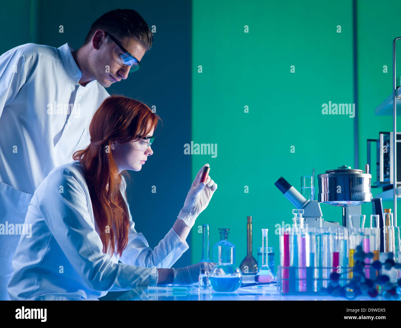 Seitenansicht der zwei kaukasischen forensische Wissenschaftler betrachten eine rote Patrone mit Fingerabdrücken auf, in einem Labor Stockfoto