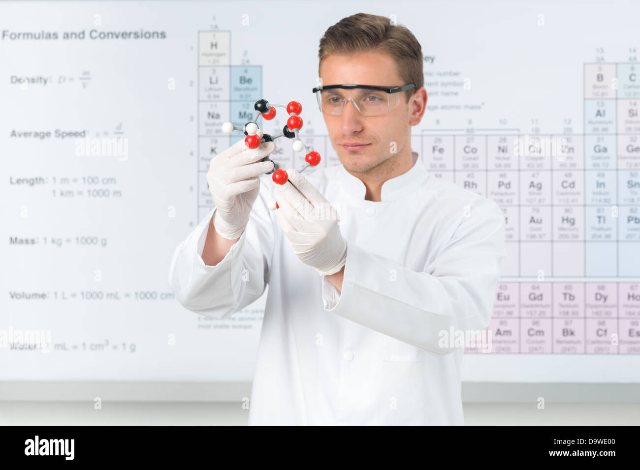 Nahaufnahme des schönen kaukasischen Wissenschaftlers gekleidet in weißen Uniform Studium molekulare Struktur mit Periodensystem im Hintergrund Stockfoto