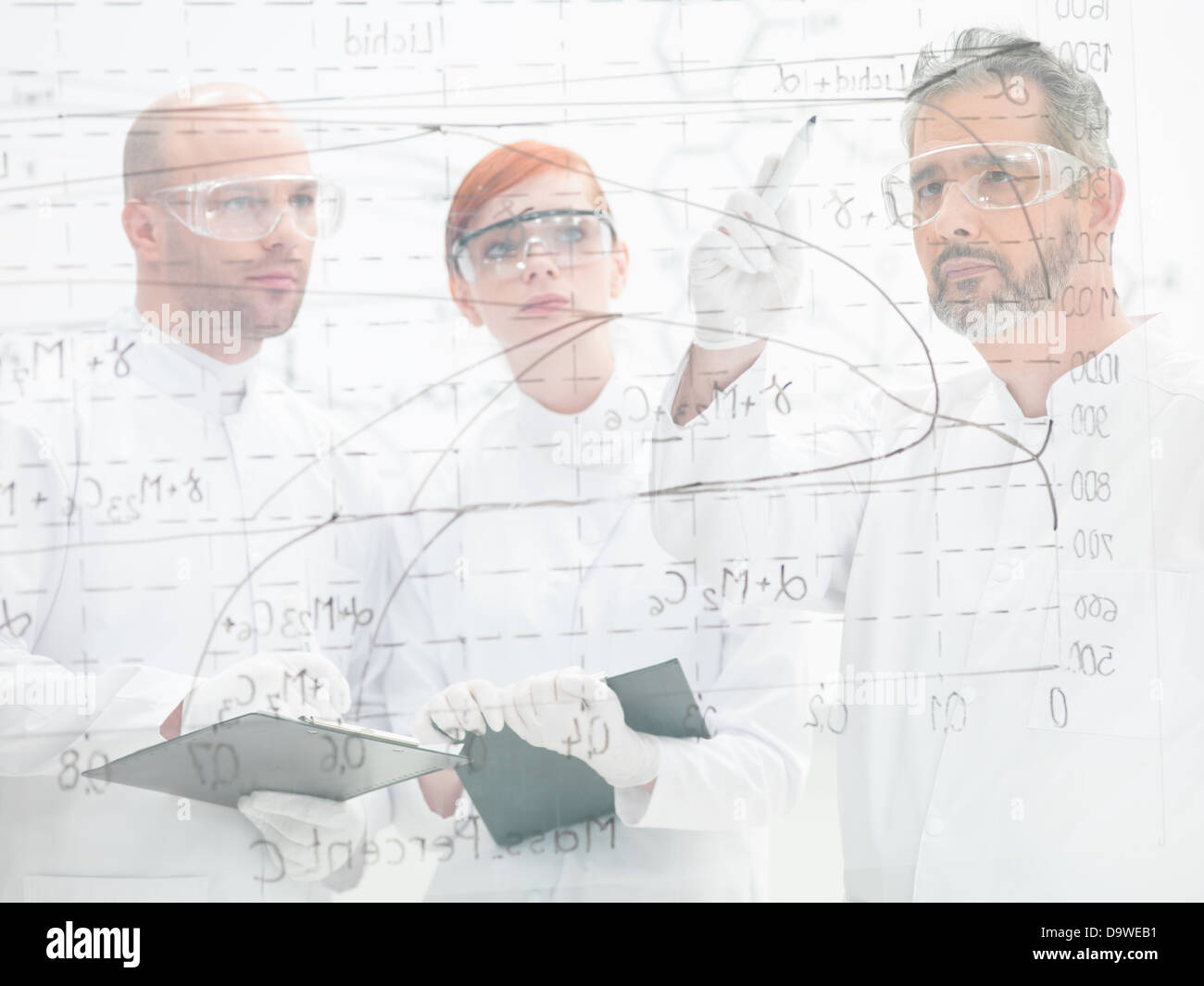Drei Wissenschaftler stehen ein Diagramm zu diskutieren und analysieren die Ergebnisse eines Experiments auf einer Glas-Oberfläche, sie sind dahinter Stockfoto