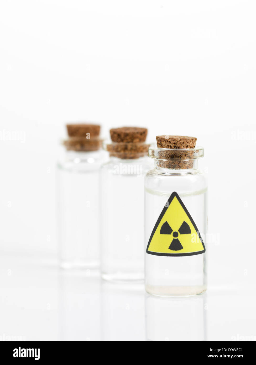 weißen Hintergrund mit drei kleinen transparenten Glasflaschen mit einem braunen Korken und ein Warnschild Radioaktivität Stockfoto