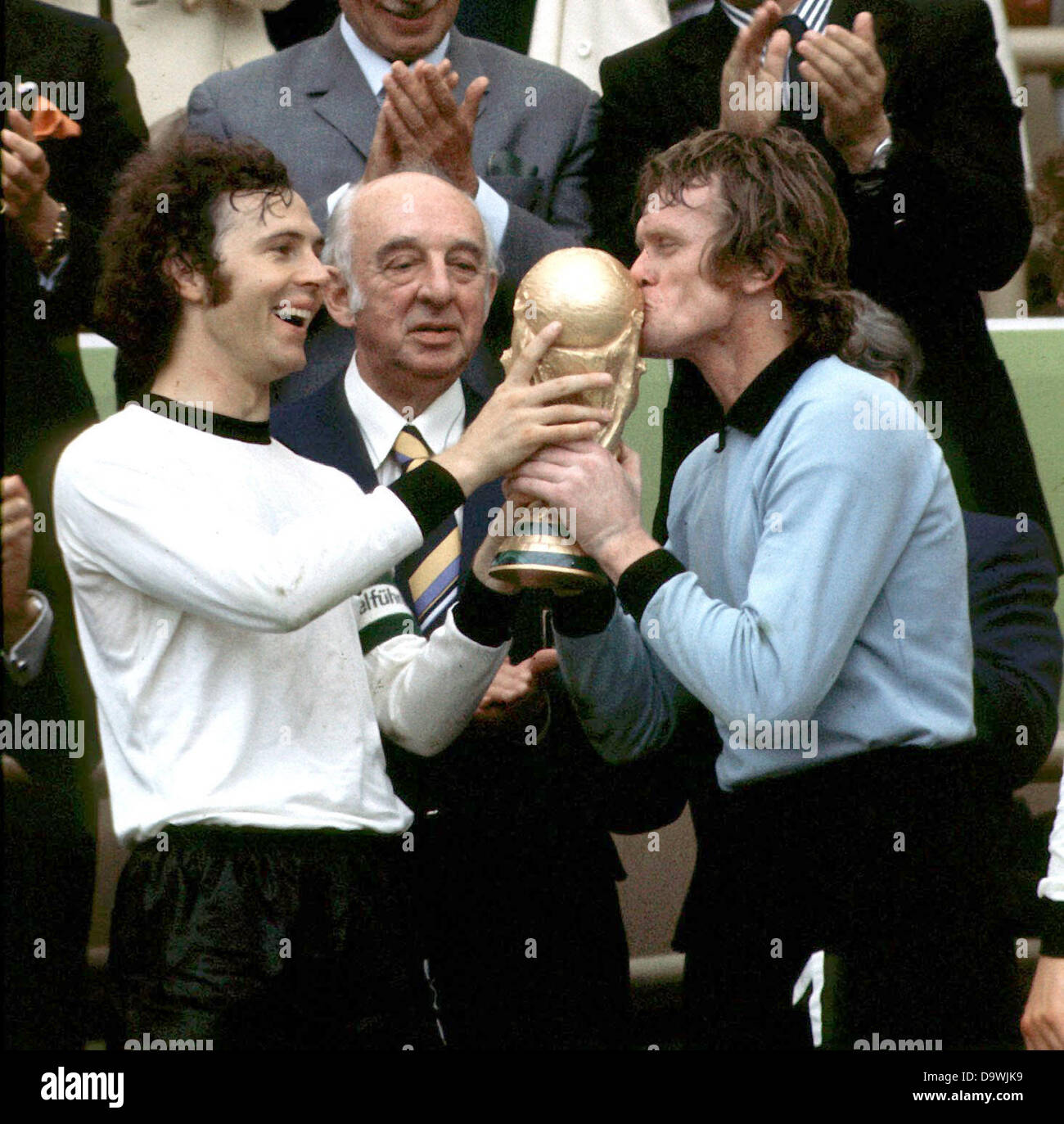 Lachende Mannschaftskapitän Franz Beckenbauer hält eroberten WM-Pokal und Torwart Sepp Maier ist die Trophäe zu küssen. DFB-Präsident Hermann Goessmann beobachtet. Die deutsche Fußball-Nationalmannschaft gewinnt das 1974 FIFA World Cup Finale 2:1 gegen die Niederlande im Münchner Olympiastadion in Deutschland. Stockfoto