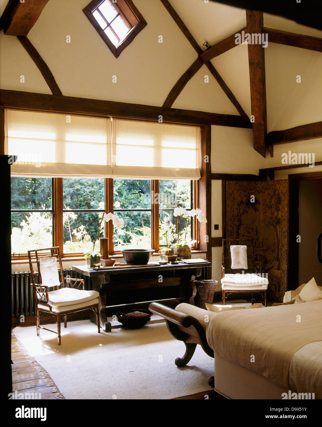 Tudor-Stil Balken und hohen Gewölbedecke im Land Schlafzimmer mit weißen blinden Fenster oben antiker Tisch Stockfoto