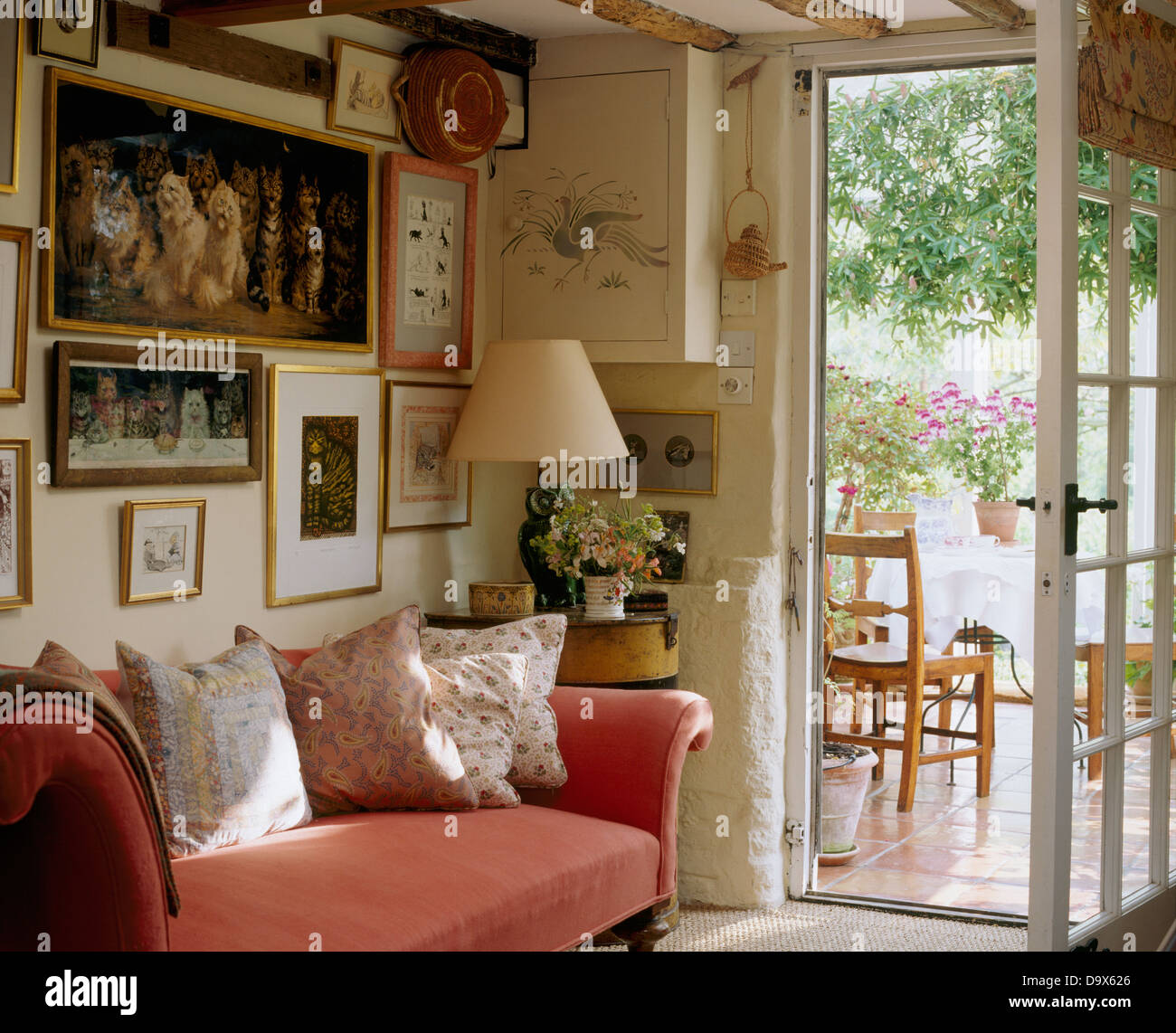 Ferienhaus Wohn-Esszimmer mit Anzeige von Bildern über rosa Sofa mit floralen Kissen neben offenen Glastür zur Terrasse Stockfoto