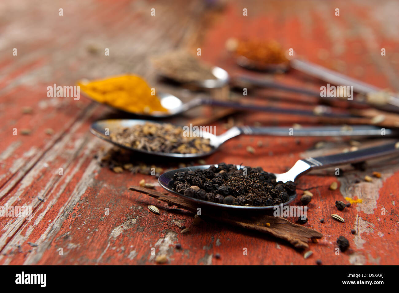 Esslöffel gehäuft mit verschiedenen Gewürzen auf eine orange Strukturierte Holzoberfläche. Künstlerische Nutzung der geringen Schärfentiefe. Stockfoto