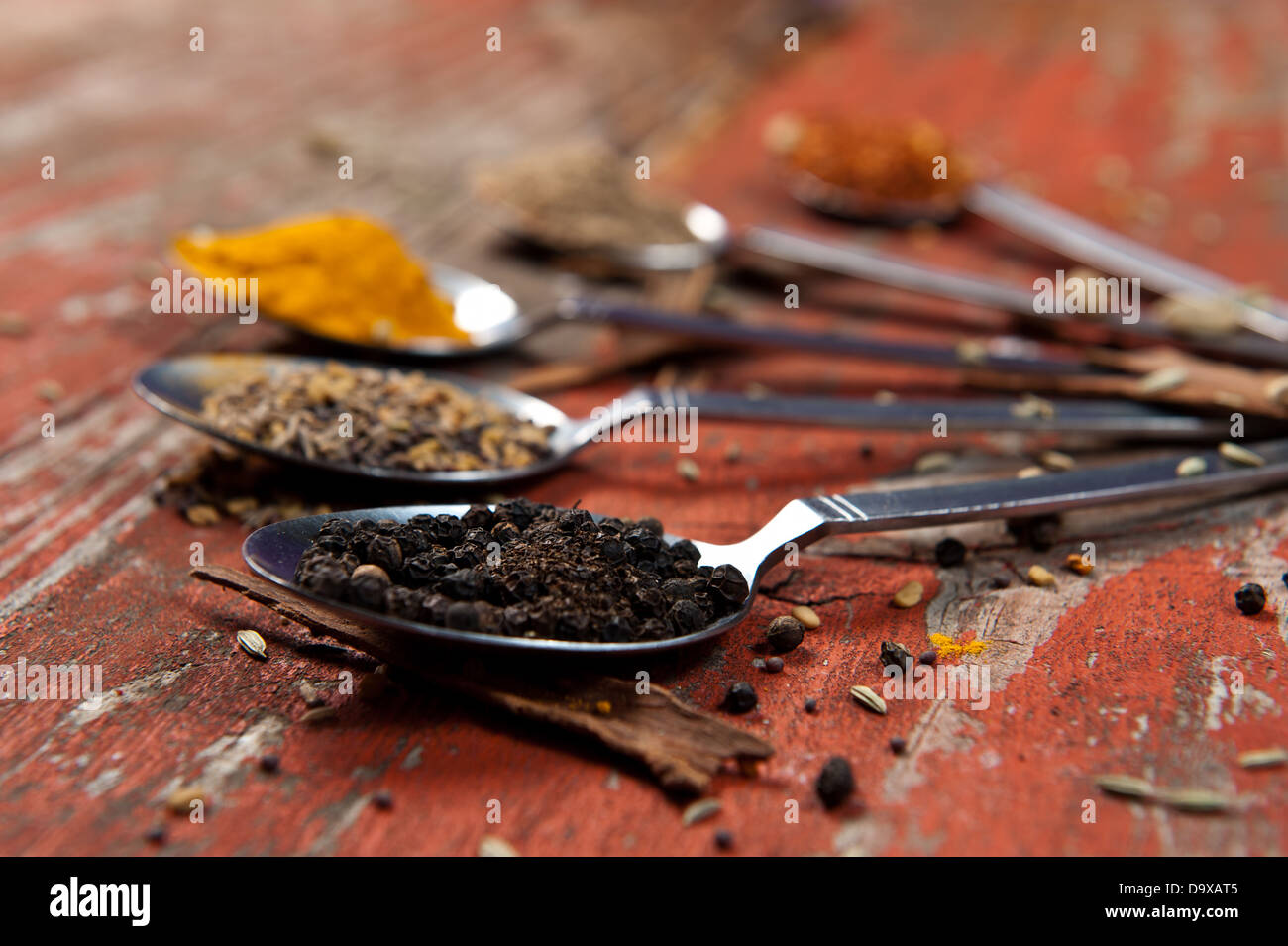 Esslöffel gehäuft mit verschiedenen Gewürzen auf eine orange Strukturierte Holzoberfläche. Künstlerische Nutzung der geringen Schärfentiefe. Stockfoto