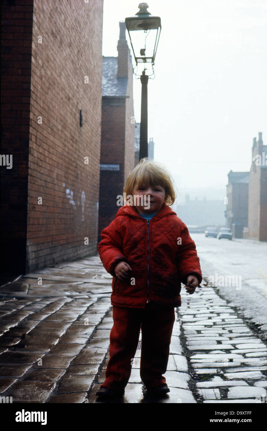 Ein kleines Kind in den 1970er Jahren in der Nähe von einem Gas Laterne in einer alten Straße mit Kopfsteinpflaster in Leeds West Yorkshire 1974 KATHY DEWITT Stockfoto