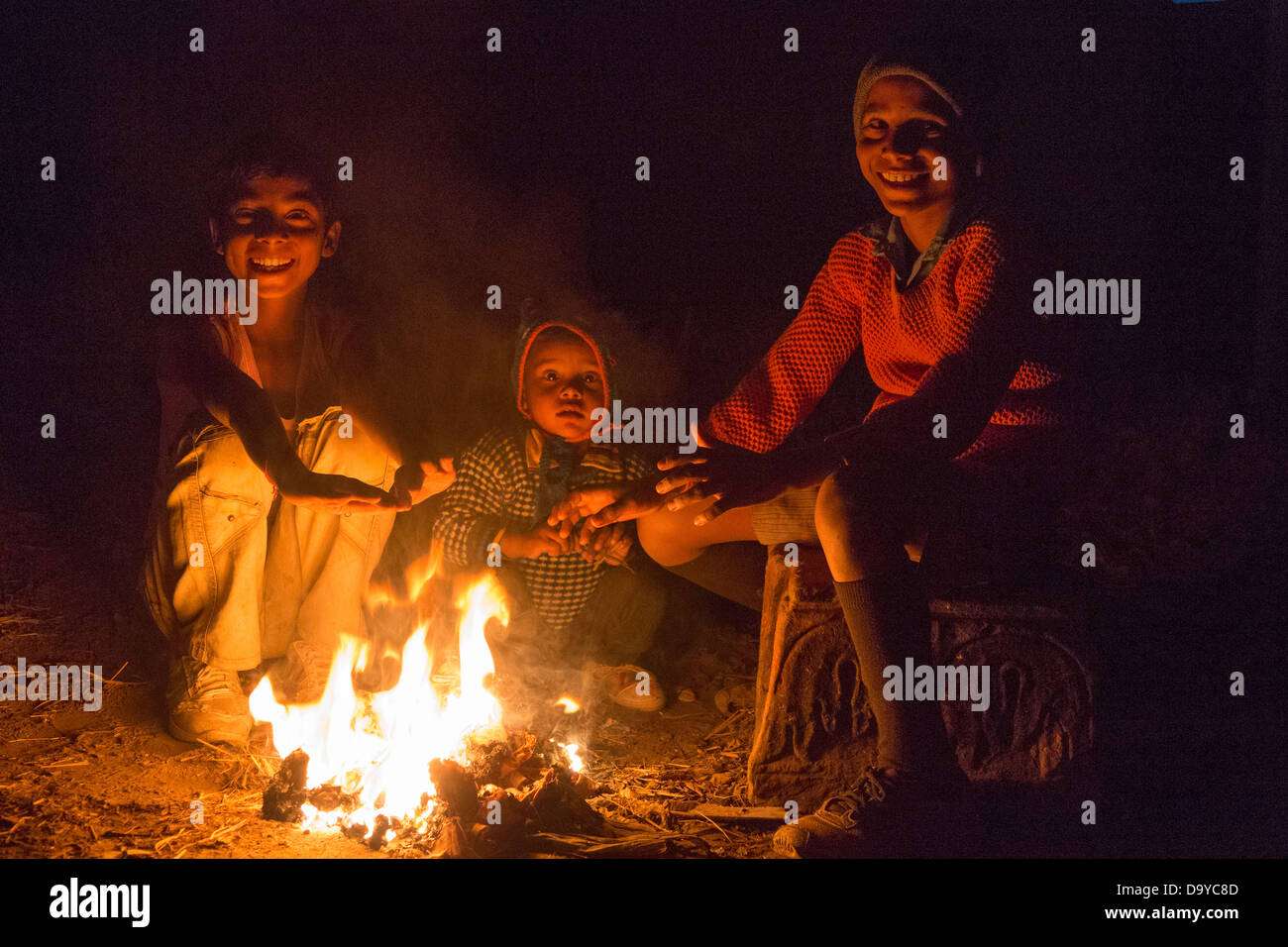 Indien, Uttar Pradesh, Agra, drei Kinder sitzen um Feuer in der Nacht Stockfoto