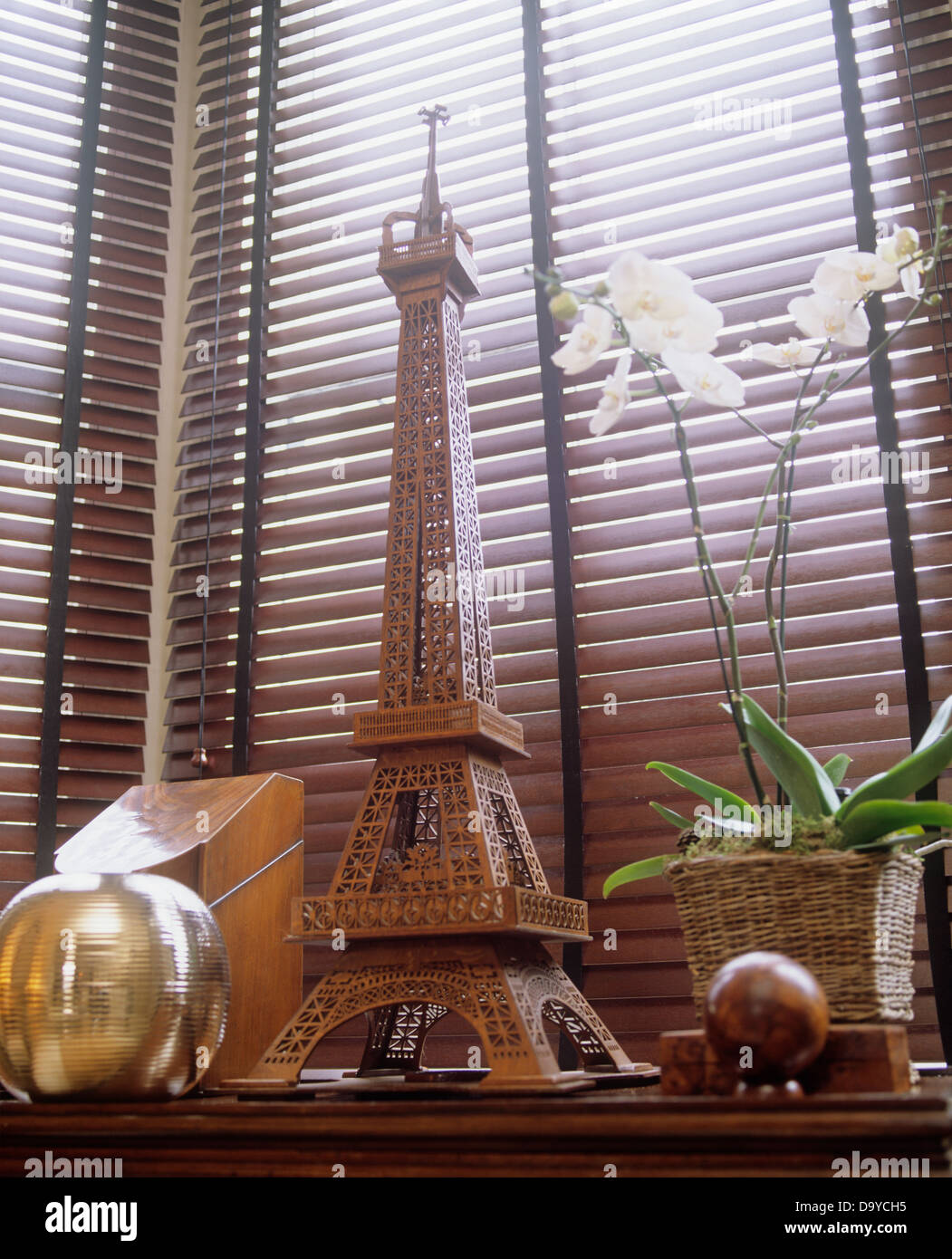 Modell des Eiffelturms mit weißen Orchideen in Wicker Topf auf Tisch mit hölzernen Gegenständen gegen Lattenrost aus Holz blind Stockfoto