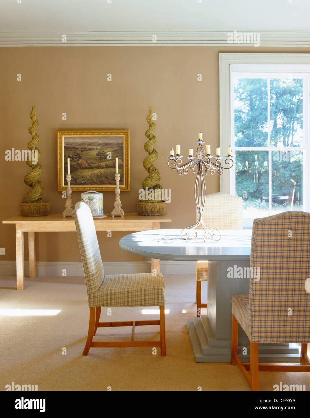 Gepolsterte Stühle an modernen ovalen Tisch in Beige Land Speisesaal mit faux Hecke auf Konsolentisch überprüft Stockfoto