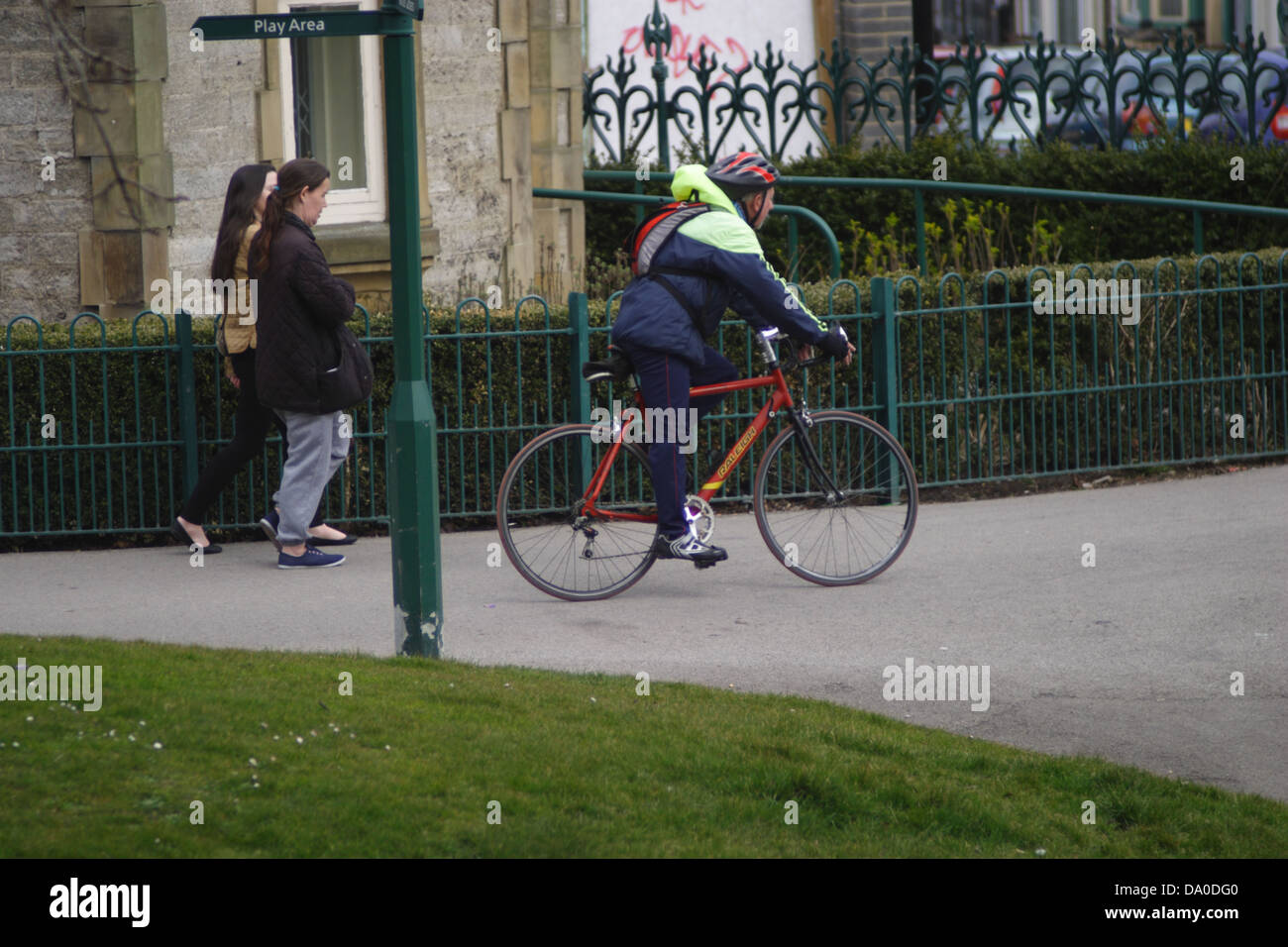 Radfahrer mit dem Fahrrad. Mann trägt einen blauen und weißen Mantel, Rucksack und Zyklus Helm. . Zwei Frauen sind hinter sichtbar. Stockfoto