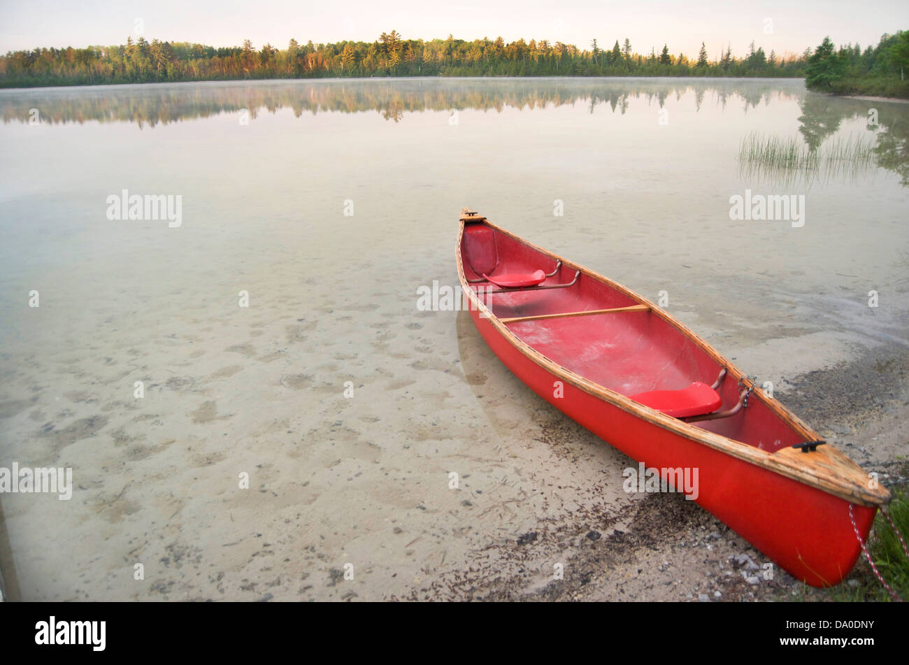 Rote Kanu bei Tagesanbruch gestrandet auf einem Binnensee. Stockfoto
