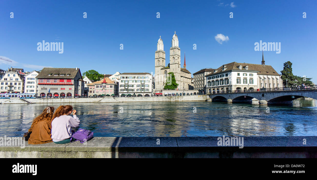 Grossmünster Kathedral, 2 Mädchen sitzen am Fluss Limmat, Zürich, Schweiz Stockfoto