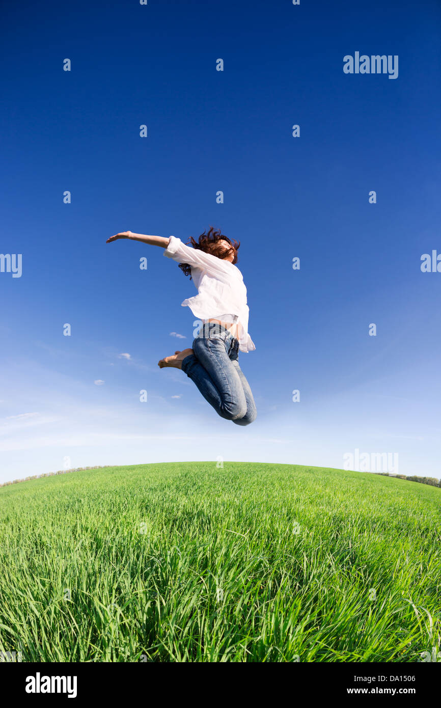 Glückliche Frau im grünen Feld gegen blauen Himmel springen. Sommer Urlaub Konzept Stockfoto