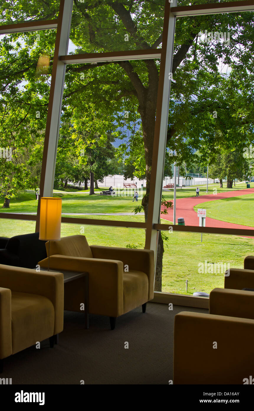 Blick auf ein Feld im Confederation Park von Burnaby-Bibliothek.  Stühle-Silhouette gegen ein Fenster mit Park und die Berge. Stockfoto