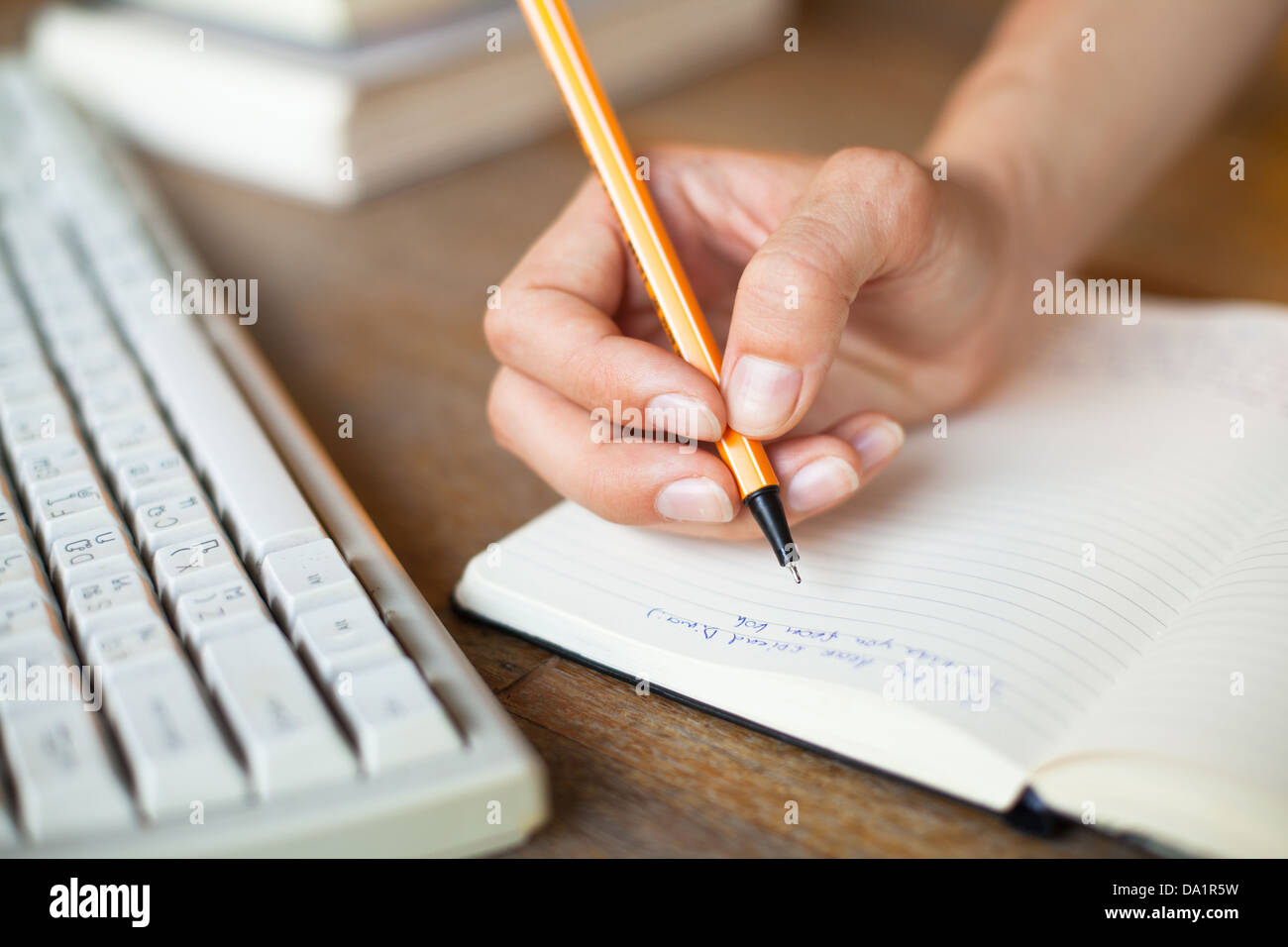 Händen schreibt einen Stift in einem Notebook, Computer-Tastatur im Hintergrund Stockfoto