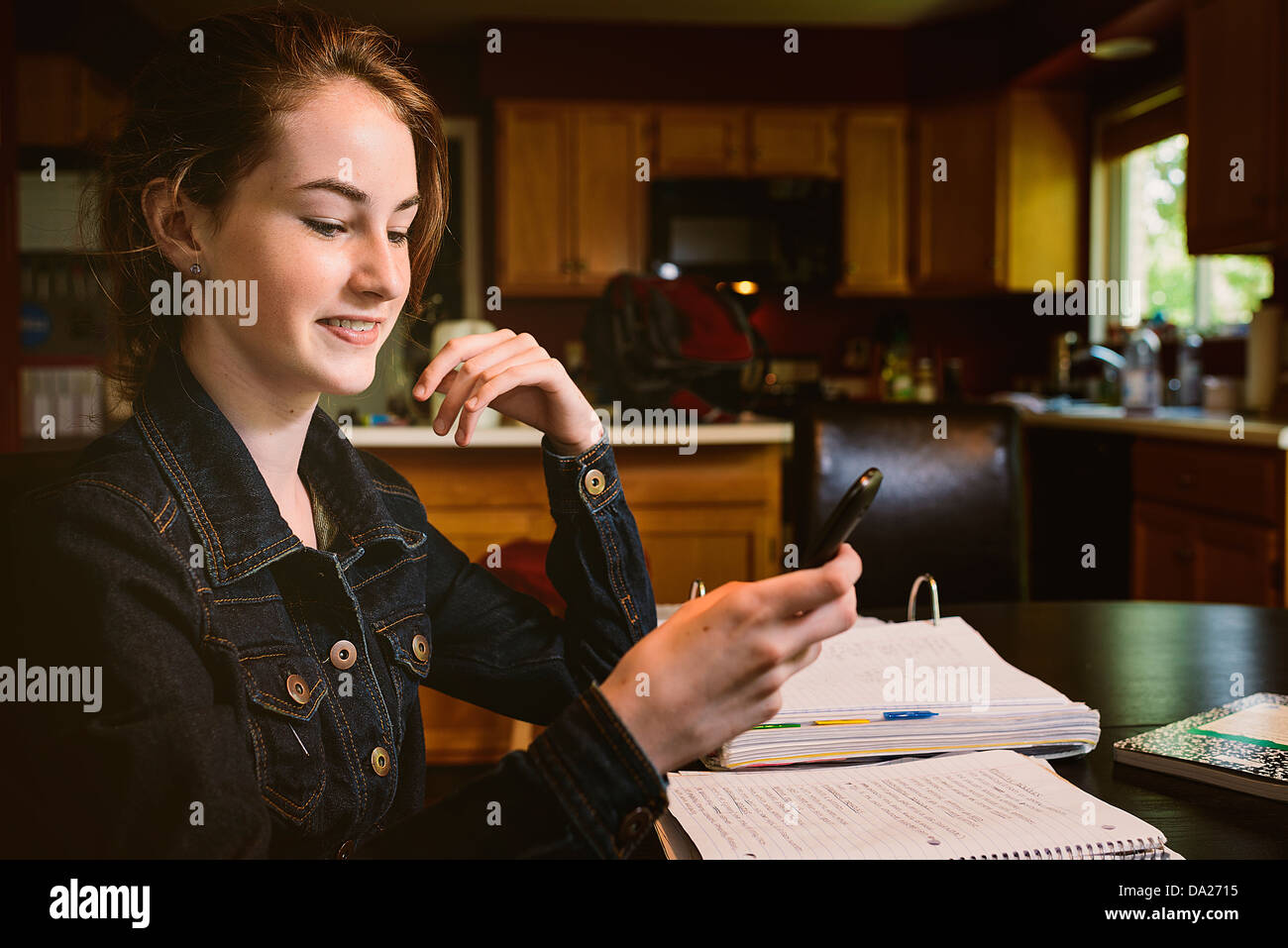 Junges Mädchen am familiären Küchentisch studiert und erforscht etwas auf ihrem Handy Stockfoto