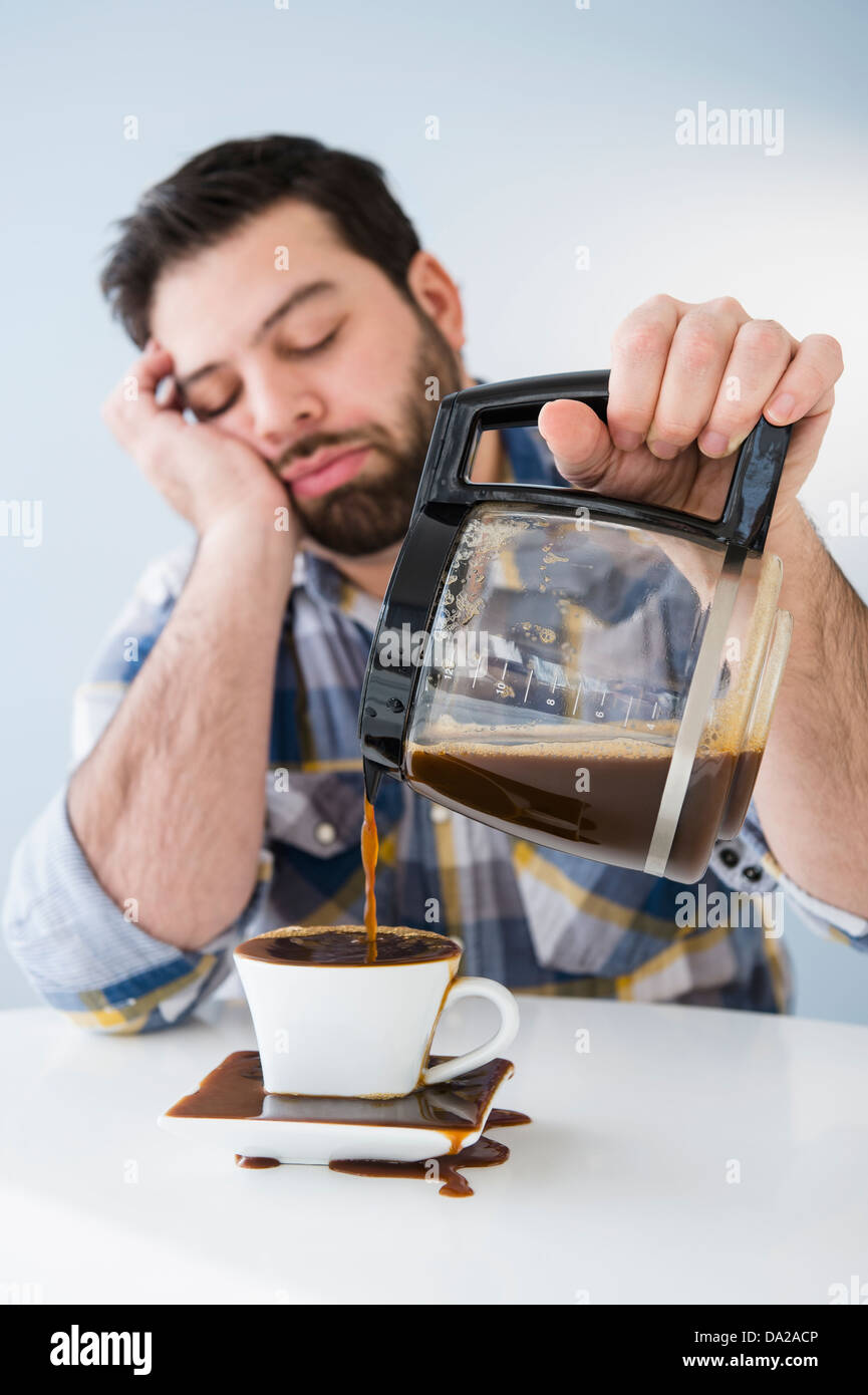 Müde, müde Mann verschüttet Kaffee am Tisch Stockfoto