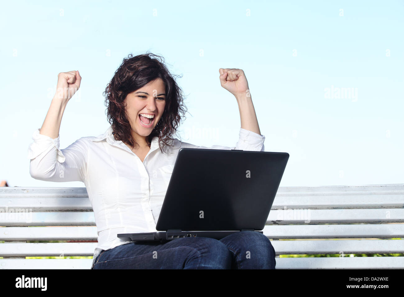 Euphorische Geschäftsfrau mit einem Laptop sitzen auf einer Bank mit dem Himmel im Hintergrund Stockfoto