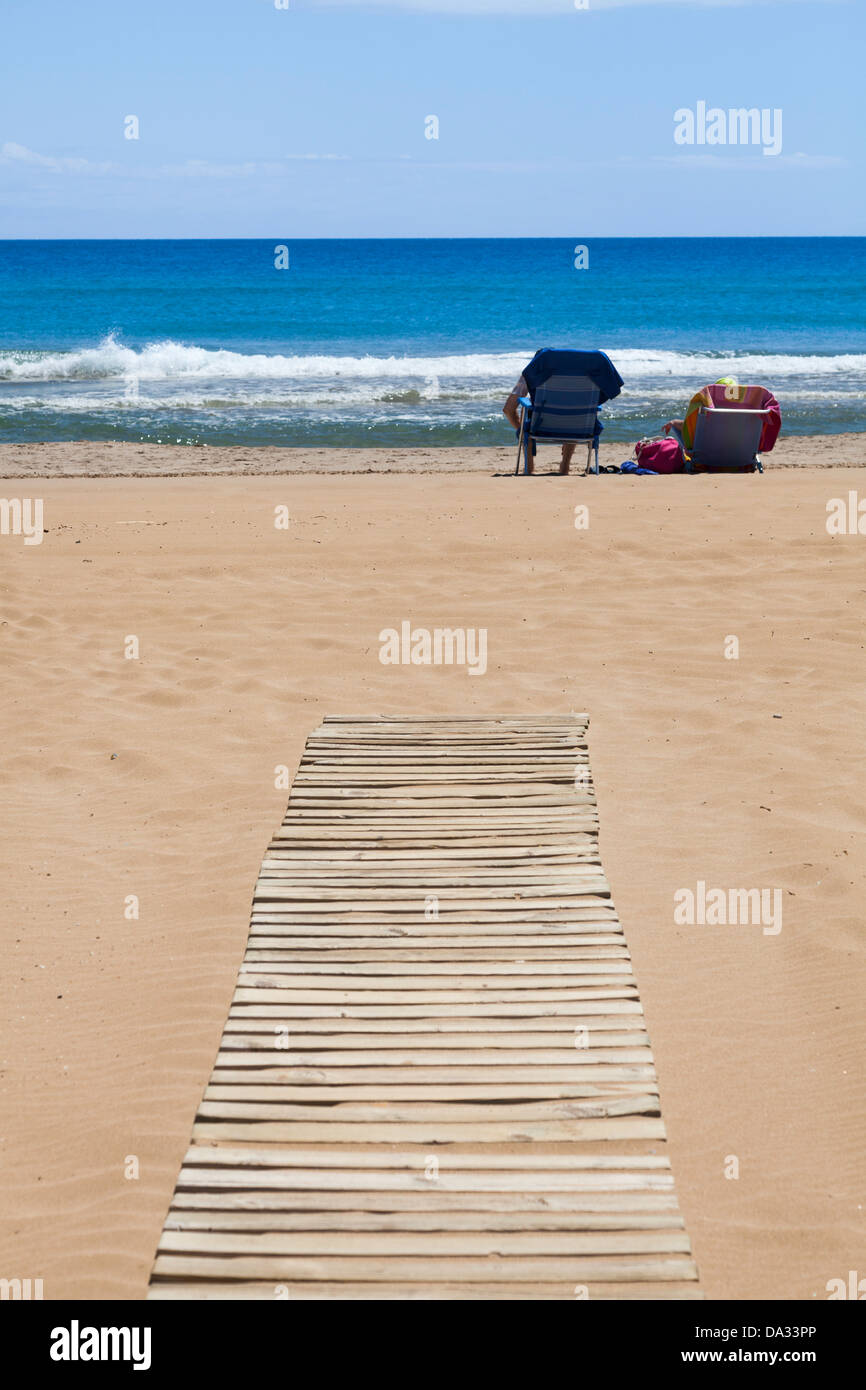 Menschen in Liegestühlen am Ende der Holzlatte Rollstuhlrampe Strand Zugang Stockfoto