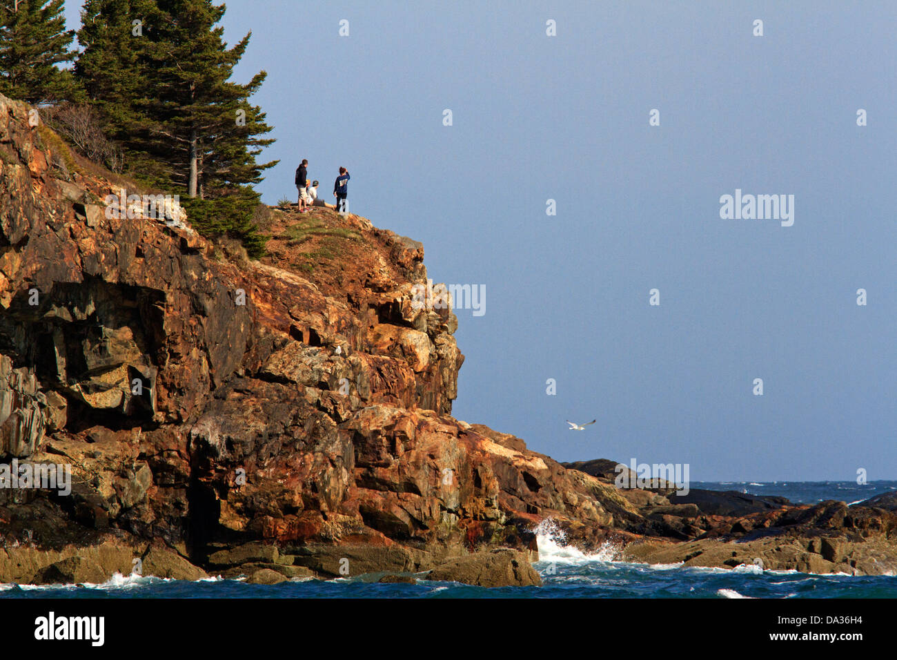 Drei Personen stehen auf einer Klippe am Strand mit Sand, Acadia, Nationalpark, Maine. Stockfoto