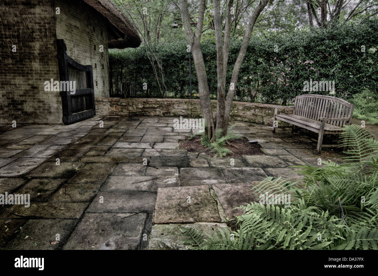 Dieses Bild ist eine Holzbank in einem üppigen Garten mit Bäumen und Pflanzen. Es ist ein Stein Gehweg und Tor auf der Bank. Stockfoto