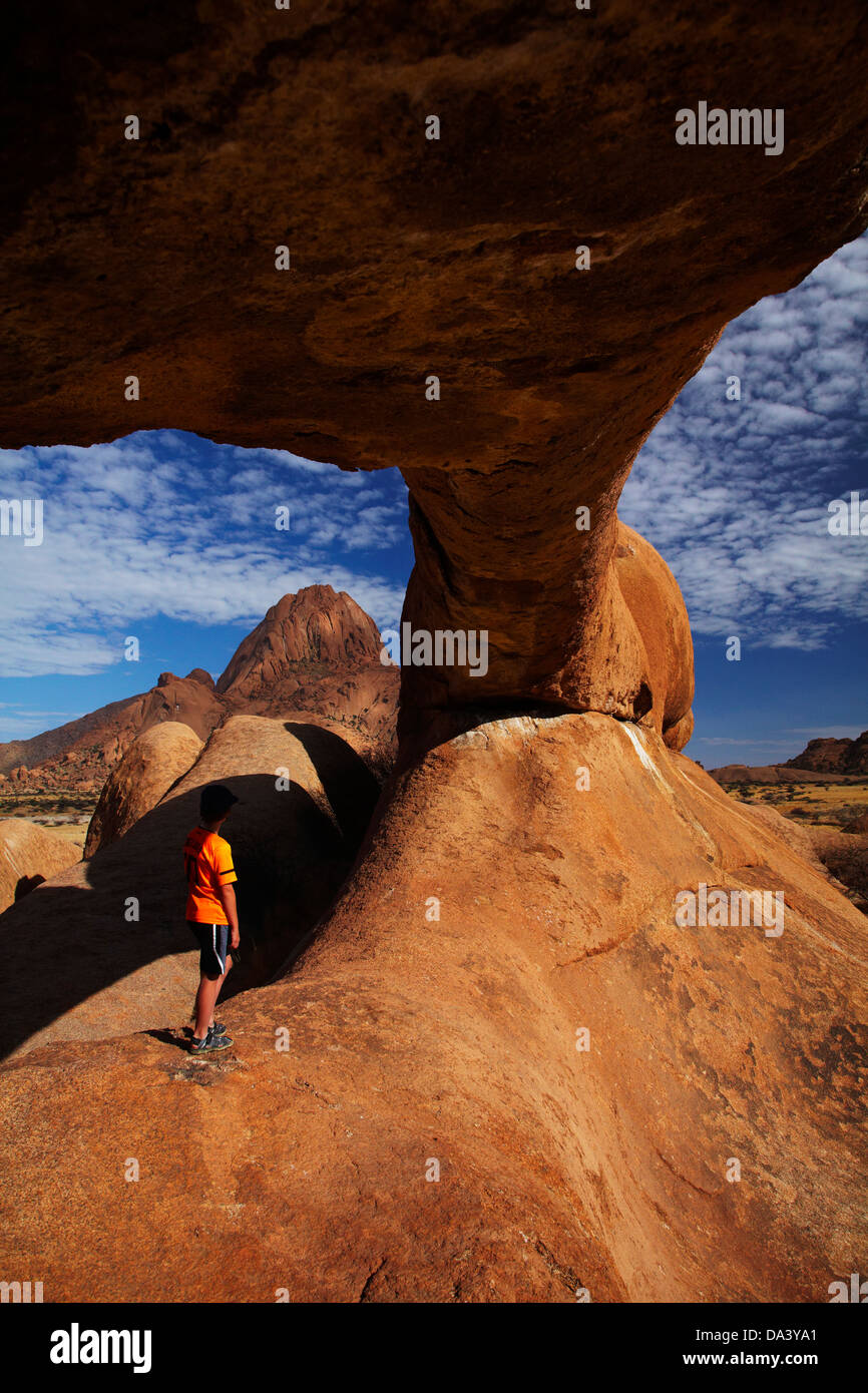 Junge unter natürlichen Felsbogen und Spitzkoppe in Ferne, Namibia, Afrika Stockfoto