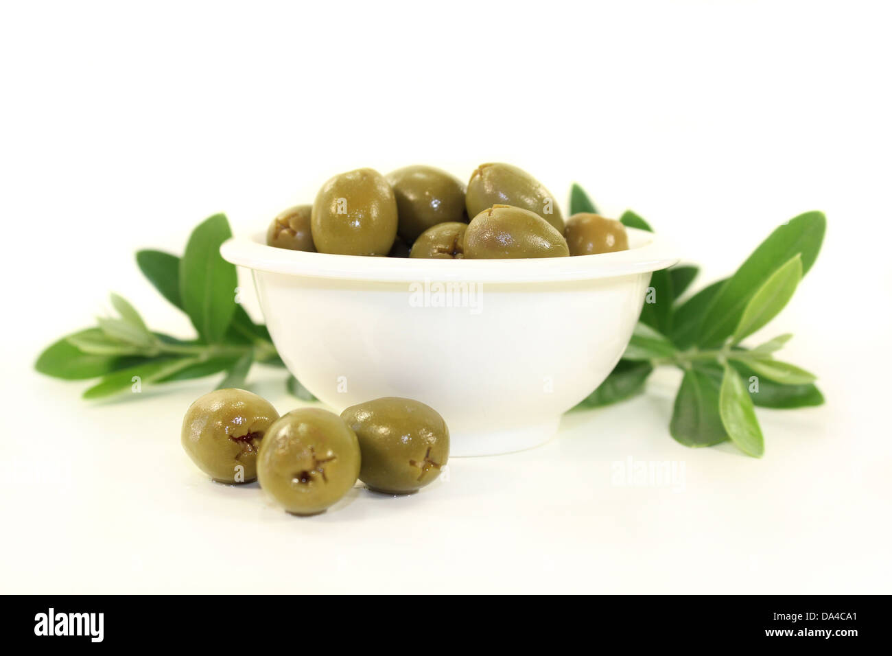 grüne Oliven und Olivenzweig in einer weißen Schüssel Stockfoto