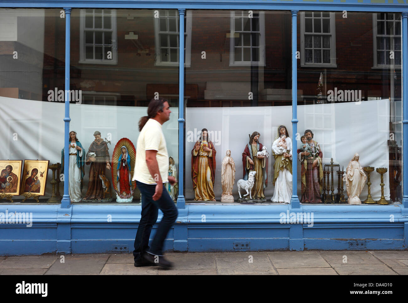 Religiöse Statuen auf dem Display in einem Schaufenster als Mann geht vorbei. Stockfoto