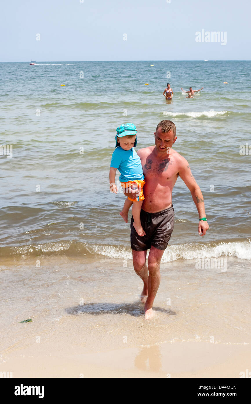 Vater trägt Baby Boy beim Paddeln im Meer Stockfoto