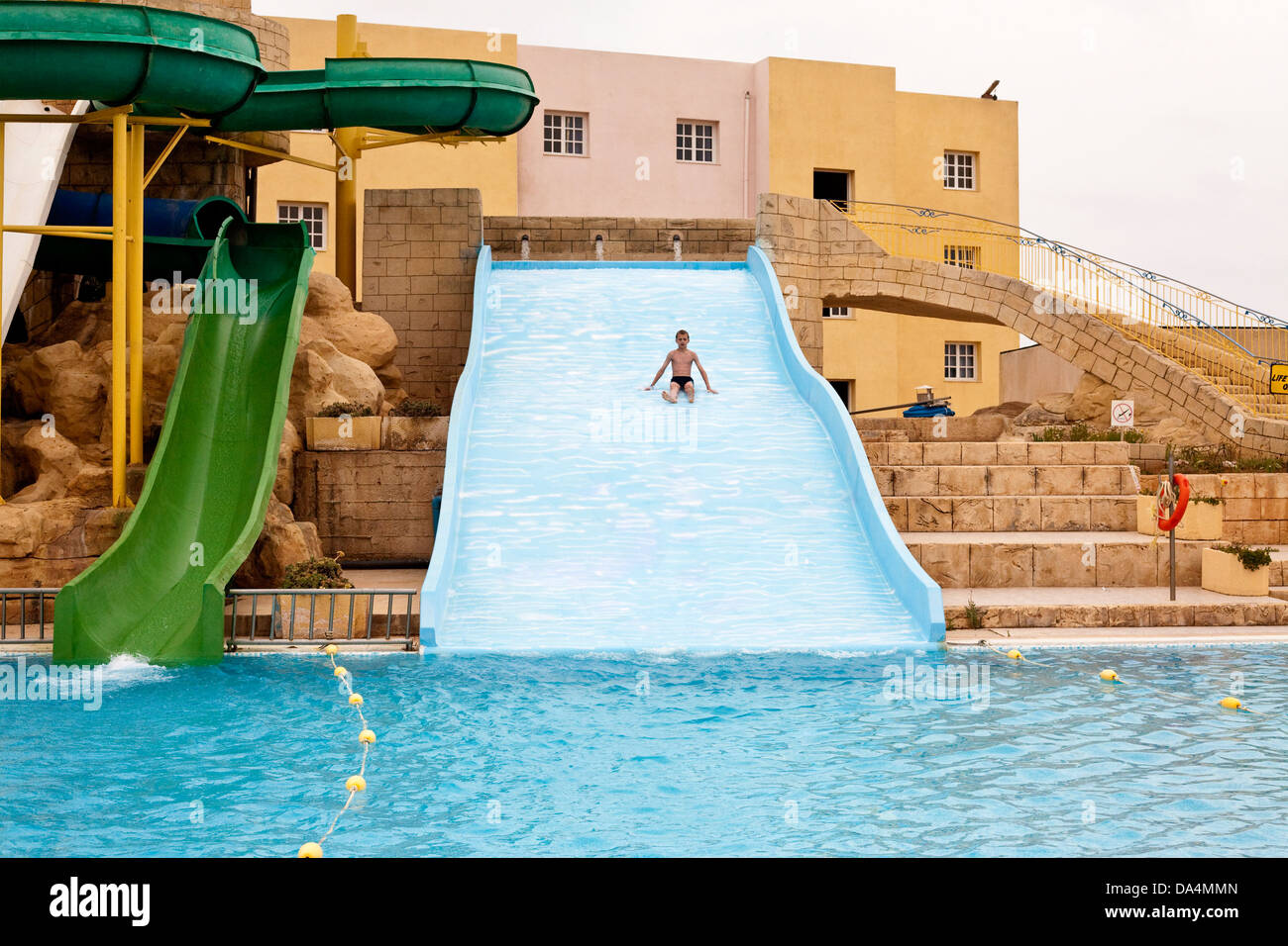 junge gleitet hinunter eine Rutsche in einen Pool in einem Wasserpark Stockfoto