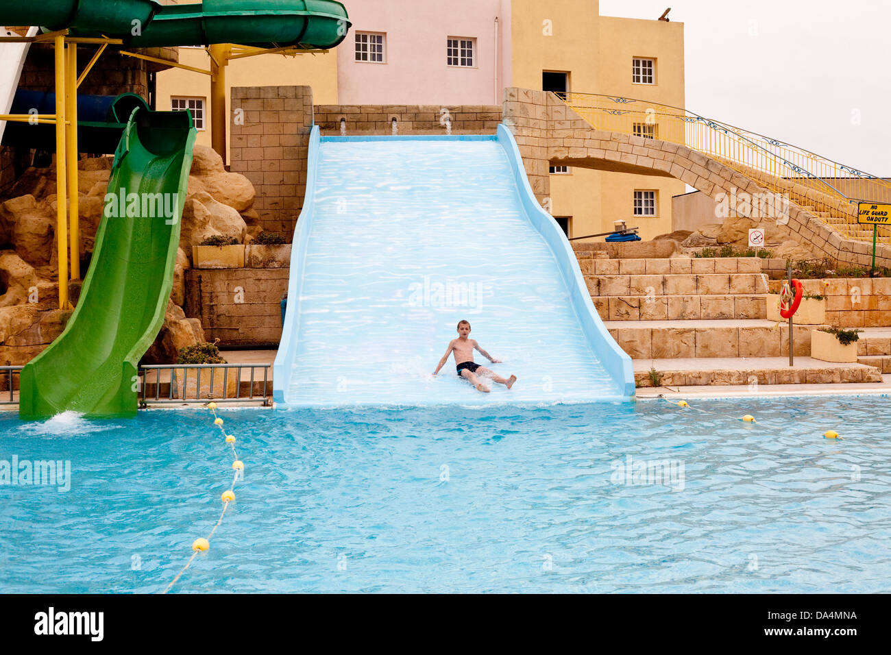 junge gleitet hinunter eine Rutsche in einen Pool in einem Wasserpark Stockfoto