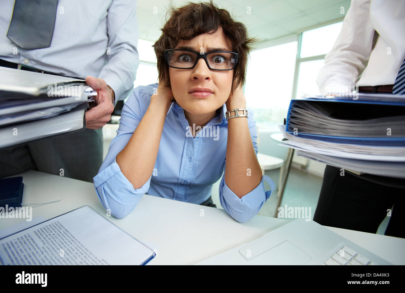 Verängstigte Sekretärin berühren den Kopf beim Blick in die Kamera, umgeben von großen Haufen von Papieren Stockfoto