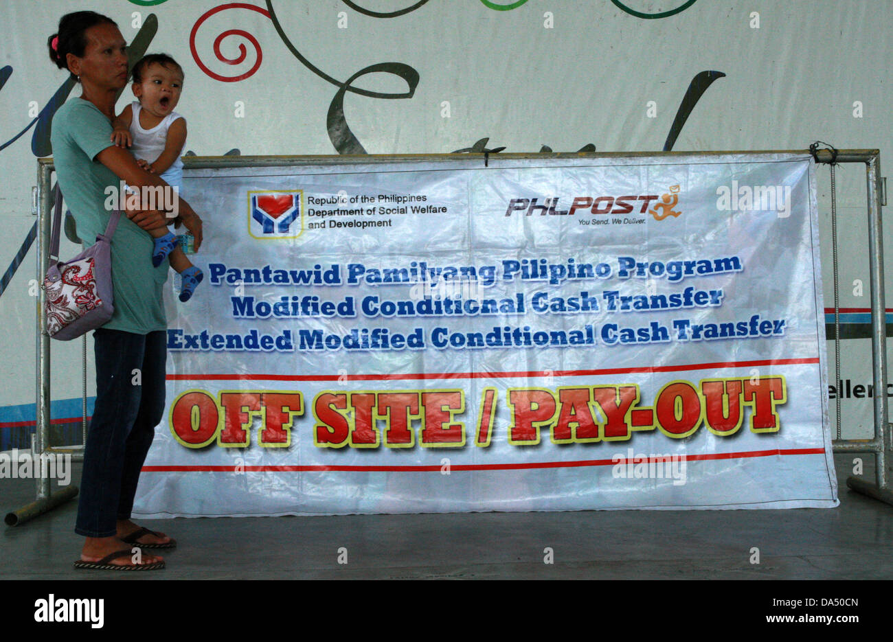 GENERAL SANTOS, Philippinen, 4. Juli 2013. Eine Mutter trägt im südlichen philippinischen General Santos, wie sie ihrerseits auf finanzielle Zuschüsse von der Regierung, 4. Juli 2013 erwartet. Unter conditional Cash Transfer Programm von Department of Social Welfare und Entwicklung stellt die Regierung monatliche Zuschüsse für ausgewählte arme Haushalte. Begünstigte sind verpflichtet, ihre Kinder in öffentlichen Schulen schicken, und die Kinder haben und die Mütter besuchen regelmäßig öffentliche Gesundheitszentren. Bildnachweis: Jeoffrey Maitem/Alamy Live-Nachrichten Stockfoto