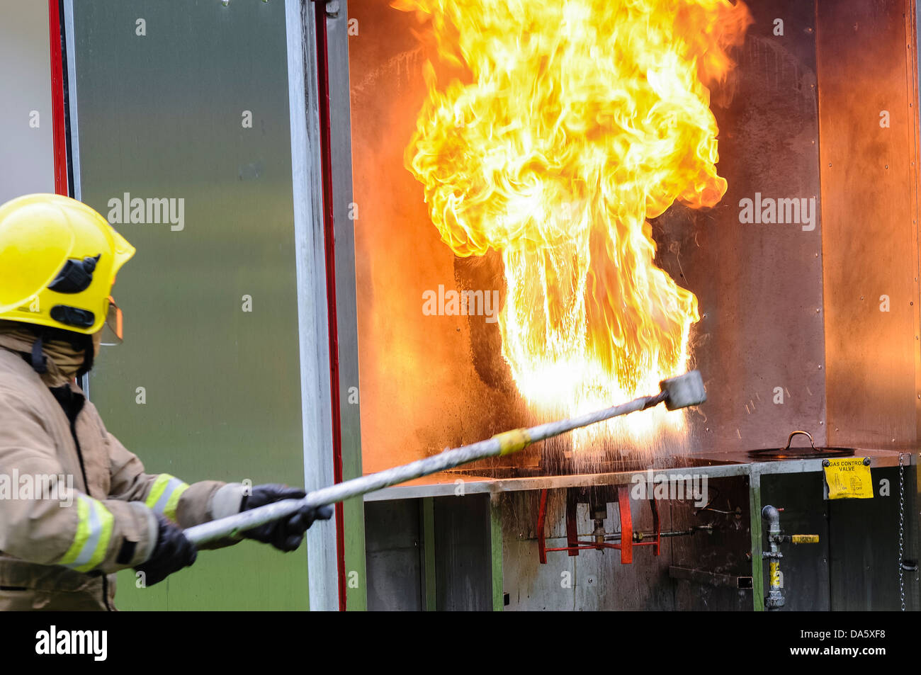Ein Feuerwehrmann zeigt das Ergebnis von Gießen eine kleine Menge Wasser auf einem brennenden Spänewanne in einer kontrollierten Umgebung Stockfoto