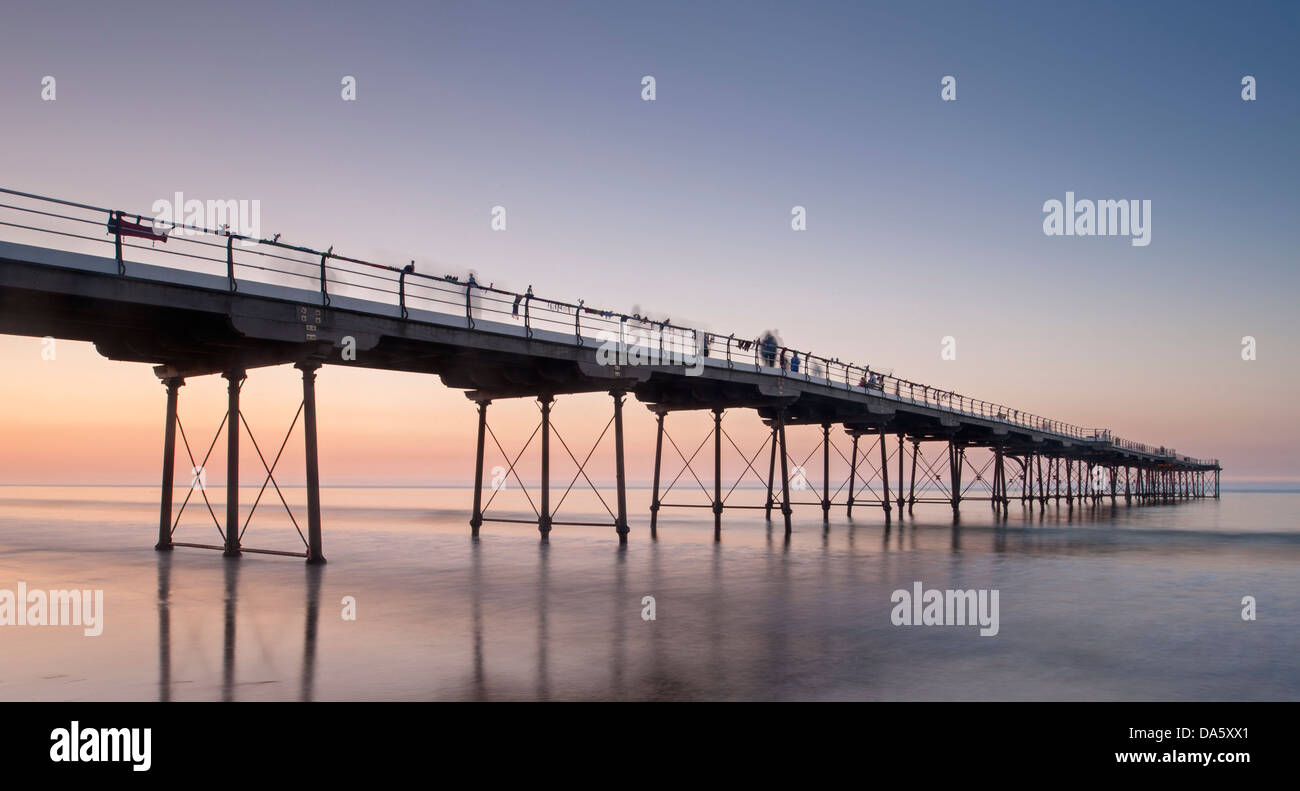 Unter bunten Sommer Sonnenuntergang Himmel, Blick vom Sandstrand von Menschen zu Fuß auf historischen Seaside pier über ruhige See - Saltburn-by-the-Sea, England, UK. Stockfoto