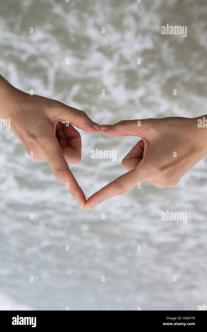 Weibliche Hände machen eine Herzform am Strand. Stockfoto