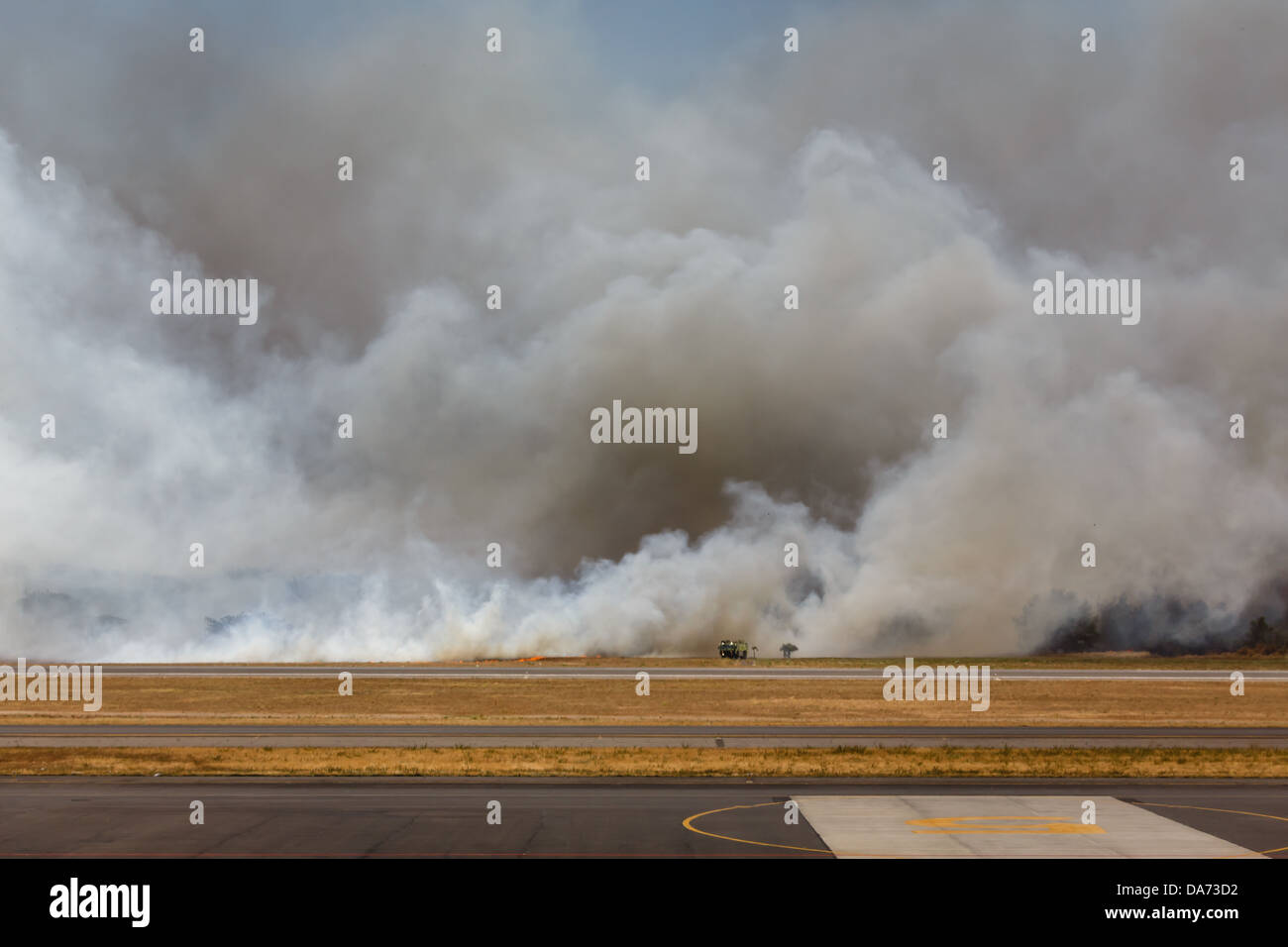 Rauch umgibt die Feuerwehr und Ausrüstung, die Bürstenfeuer bekämpfen, wodurch der internationale Flughafen San Salvador geschlossen wird Stockfoto