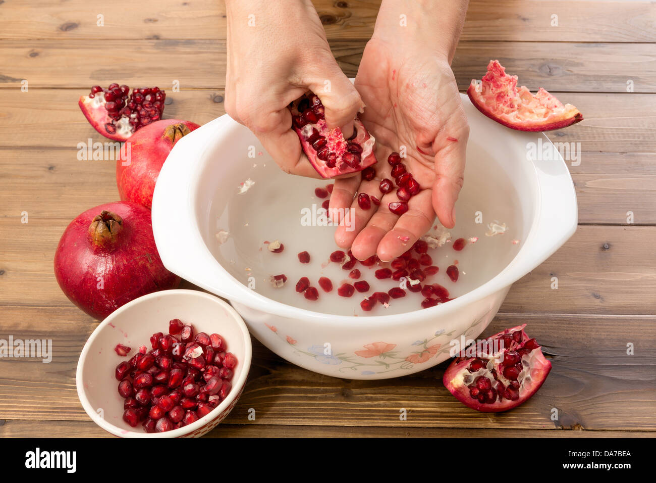 Hände, die Granatapfel-Samen in eine Schüssel mit Wasser für die Herstellung von Saft zu sammeln Stockfoto