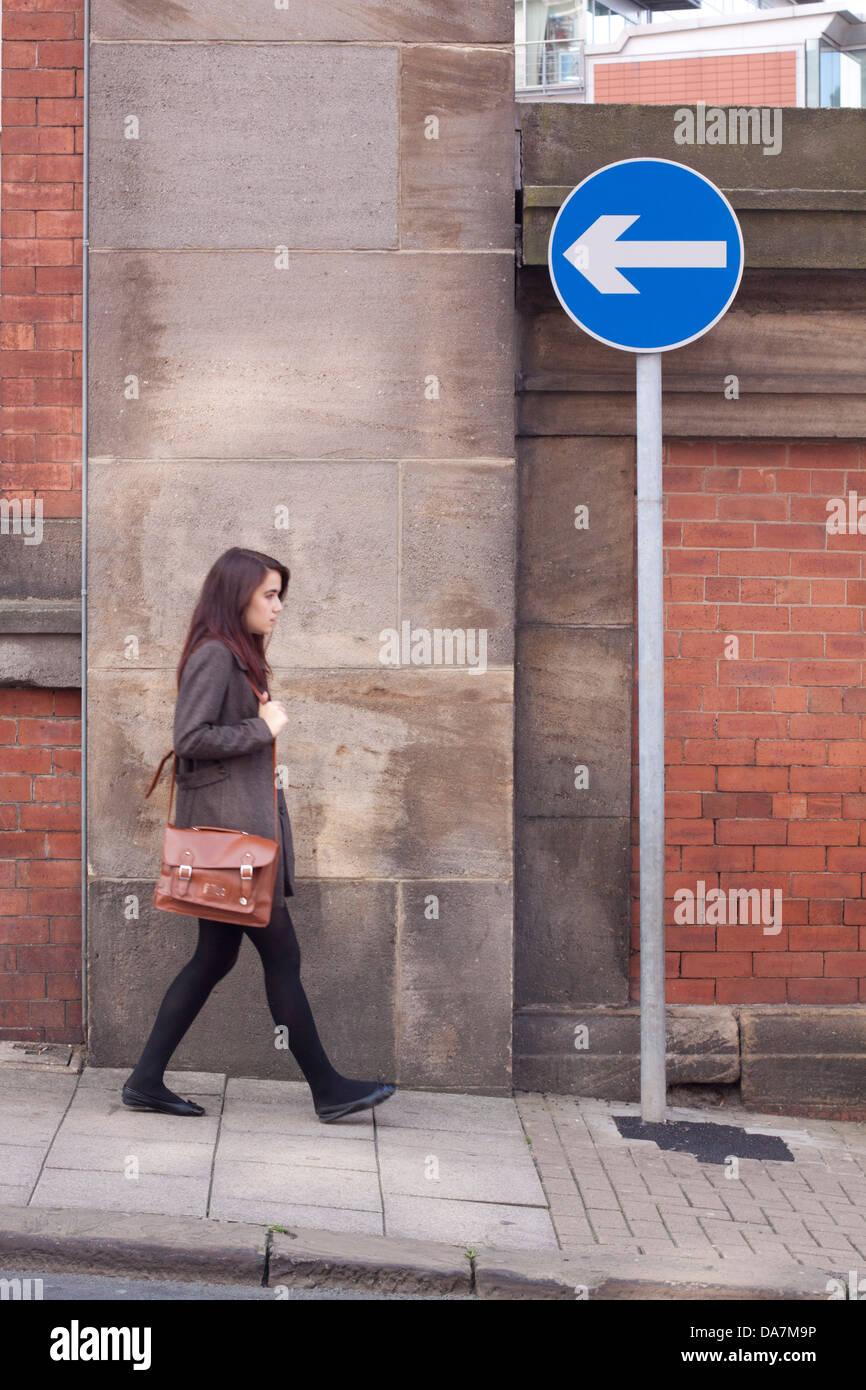 Junge Frau, die zu Fuß in die entgegengesetzte Richtung wies darauf hin durch ein Einbahnverkehr Straßenschild Stockfoto