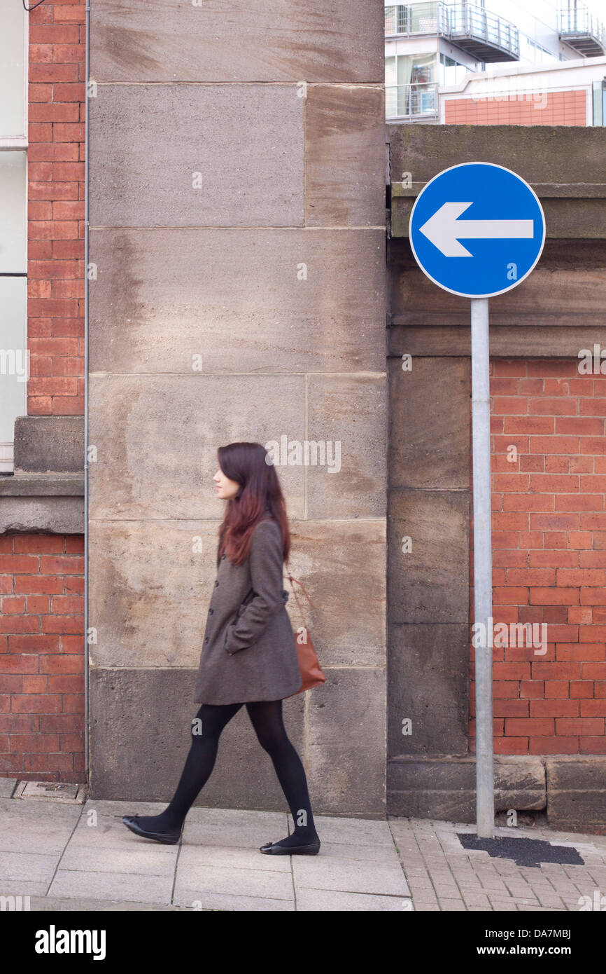 Junge Frau, die zu Fuß in Richtung verweist auf ein Einbahnverkehr Schild Stockfoto
