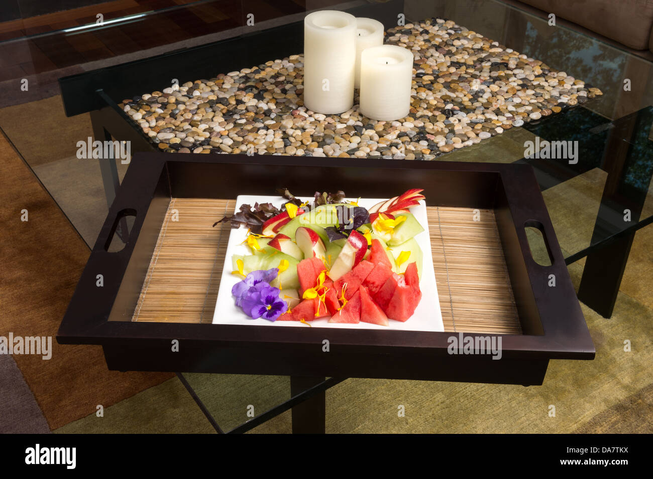 Ein Obstteller auf Bambusmatte sitzend mit Kerzen auf dem Couchtisch aus Glas Stockfoto