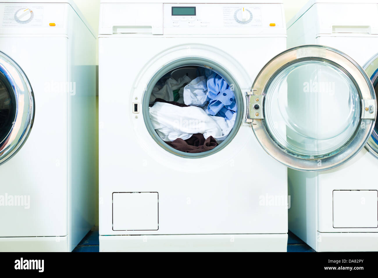 Waschküche mit Waschmaschinen nebeneinander liegt frischer Wäsche in der Trommel Stockfoto