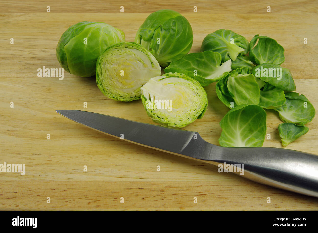 Rosenkohl geschnitten und geschält auf ein hölzernes Brett und Silber Wiegemesser Stockfoto