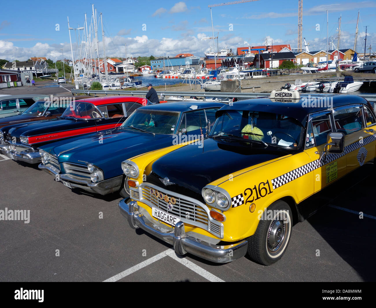 Ein Retro-Checker Taxi und Oldtimer Line-up auf einem Parkplatz in einer Marina in Schweden. Stockfoto