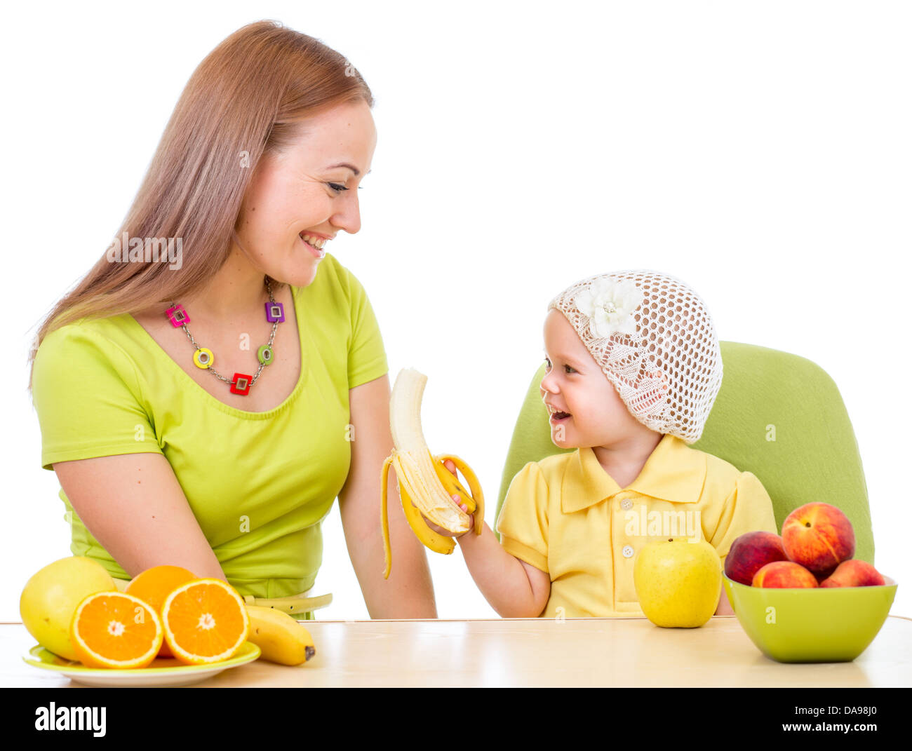 Mutter füttert kleines Mädchen mit gesunden Lebensmitteln, die am Tisch isoliert auf weiss Stockfoto
