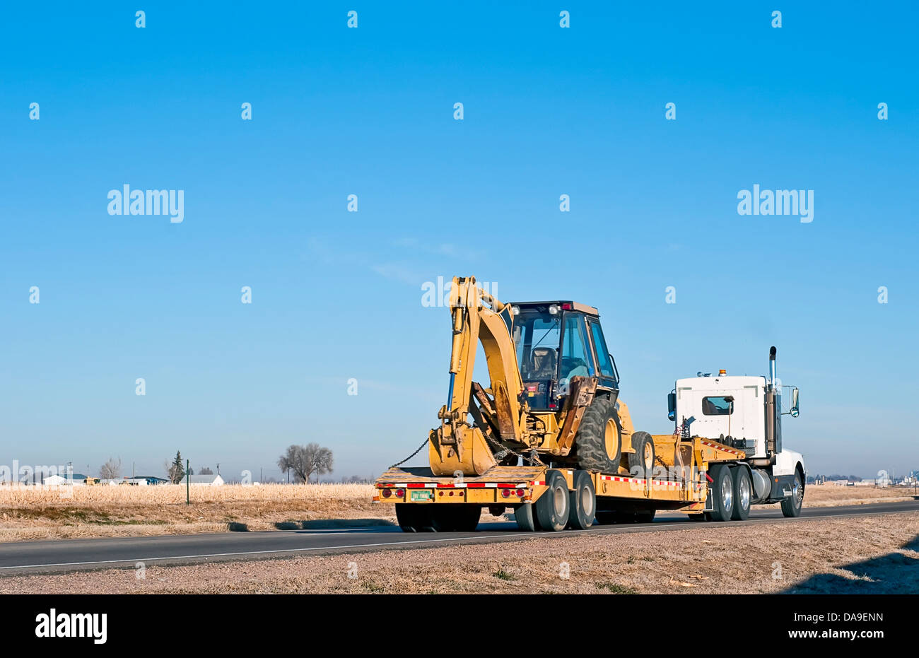 Großer LKW mit einem Drop-Deck-Anhänger schleppen einen Rücken-Hacke-Traktor. Stockfoto